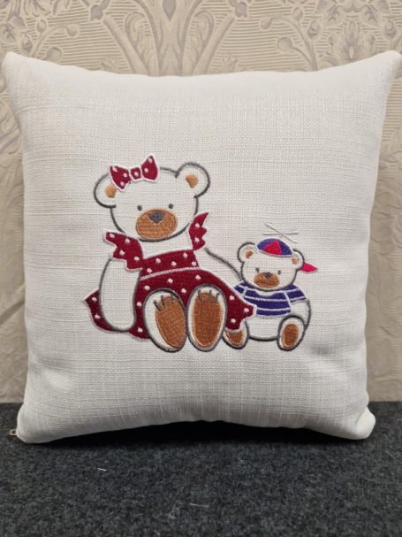 Two embroidered teddy bears, one large with a red bow and a smaller one wearing a hat.