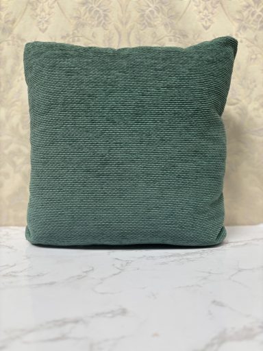 Textured green cushion on a light surface against a patterned background.