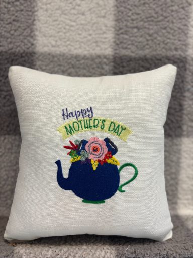 Cushion with a teapot design and "Happy Mother's Day" text surrounded by flowers.