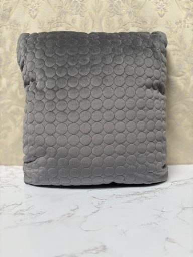 Grey cushion with a textured, circular pattern on a light marble surface.