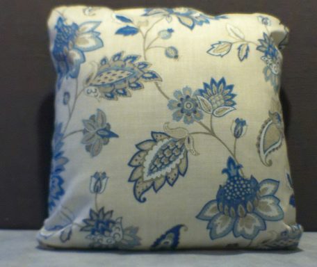 A square cushion with a blue floral and leaf pattern on a light background.