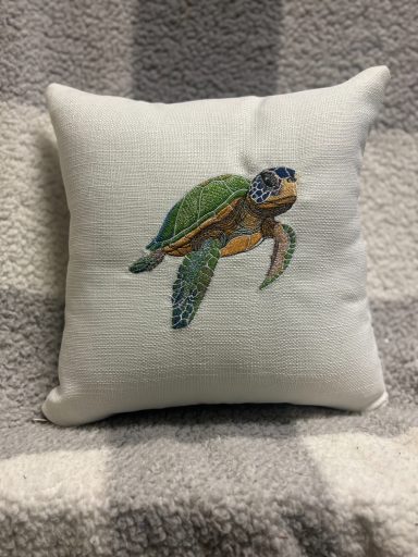 Cushion with a colourful embroidered turtle design on a light background.