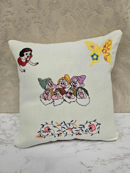 Decorative cushion featuring embroidered dwarfs and a character, with floral designs.