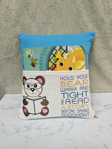 A cushion with a bear and giraffe design, featuring the text "Hold you bear warm and tight ahead."