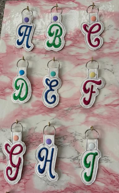 Colourful monogram keychains featuring letters A to J in decorative fonts.