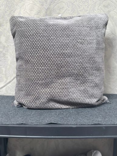 Grey textured cushion on a dark tabletop against a light wall.
