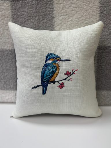 A decorative cushion featuring an embroidered kingfisher on a branch with flowers.