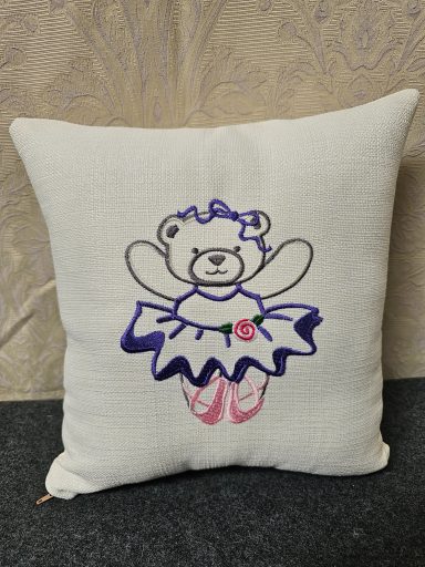 White cushion featuring a drawing of a bear in a ballet outfit.