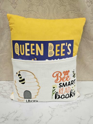 Cushion featuring a yellow and white design with bee and book-themed text.