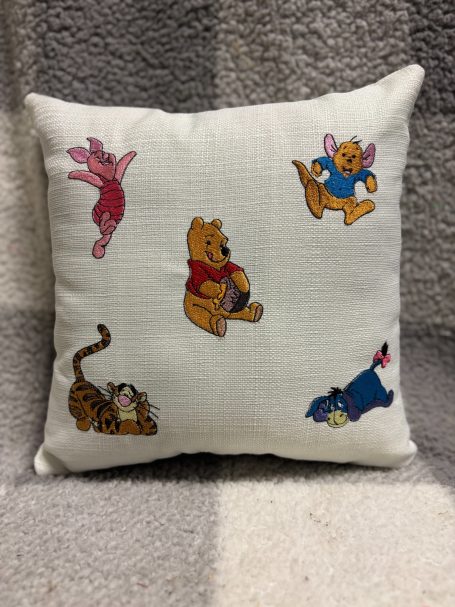 Cushion featuring playful cartoon characters: Winnie the Pooh, Piglet, Eeyore, and Tigger.