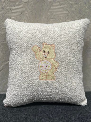 Cream cushion featuring a cartoon bear character with a happy expression and a circular emblem.