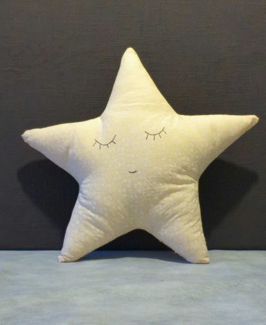A soft, cream-coloured star-shaped cushion with closed eyes and a smiling face.