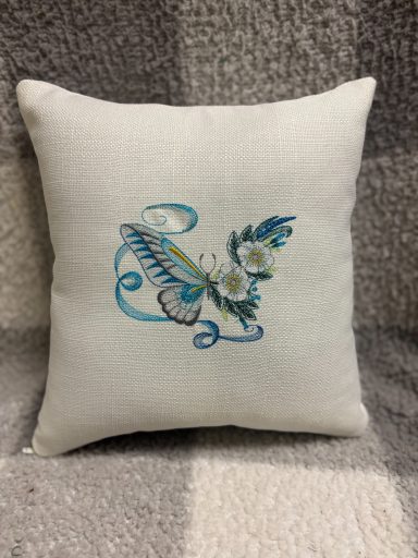 Decorative cushion with blue and green floral embroidery on a white fabric.