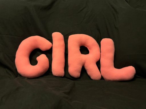 Pink plush letters spelling "GIRL" on a dark background.