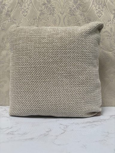 Plain beige cushion with a textured surface, positioned on a light surface.