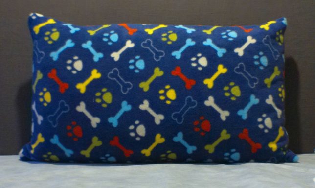 A rectangular cushion covered in a colourful pattern of bones and paw prints.