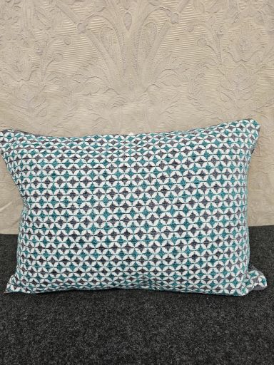 Decorative pillow with a turquoise and white geometric pattern on a grey background.