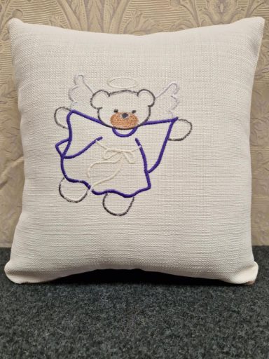 A cream cushion featuring a cartoon bear in a blue dress with angel wings.