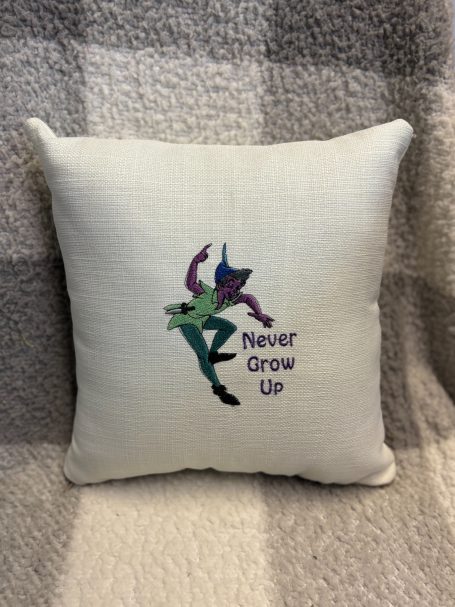 A decorative cushion with the phrase "Never Grow Up" and a whimsical character design.
