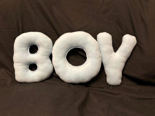 Soft, plush letters spelling "BOY" in white on a dark brown background.