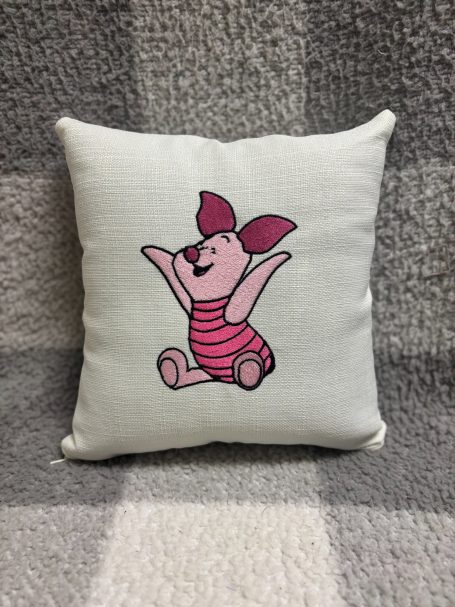Piglet A cushion featuring a playful pink pig character with ears and a striped outfit.