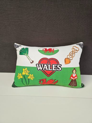 Decorative cushion featuring Welsh symbols: daffodils, a heart, and traditional icons.
