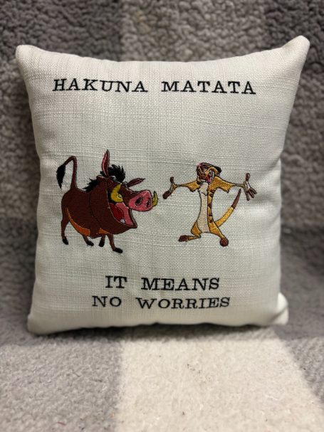 A decorative pillow featuring "Hakuna Matata" with cartoon characters Timon and Pumbaa.