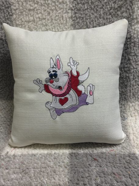 White cushion featuring a playful cartoon rabbit with a scarf and a heart.