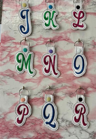 Colourful letter keychains arranged in a grid on a marble-patterned background.