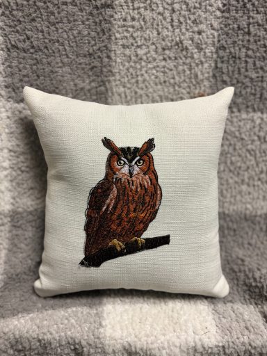 Brown owl illustration on a cream cushion, perched on a branch.