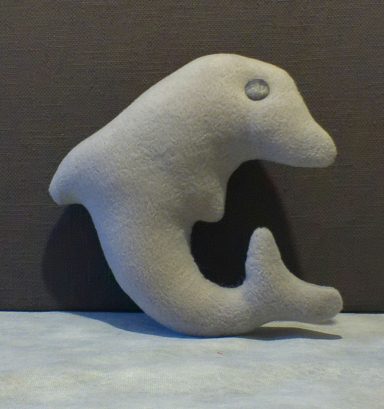 Grey plush dolphin toy with a simple, smooth design against a dark background.