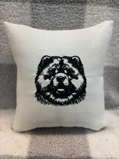 Embroidered cushion featuring a black chow chow dog's face on a white background.
