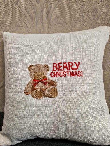 Teddy bear with a red bow and the text "BERRY CHRISTMAS!" on a cushioned fabric.