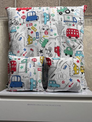 Patterned cushion featuring colourful vehicles and playful designs on a light background.
