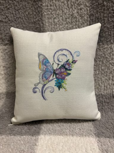Square cushion with embroidered butterfly and floral design in vibrant colours.