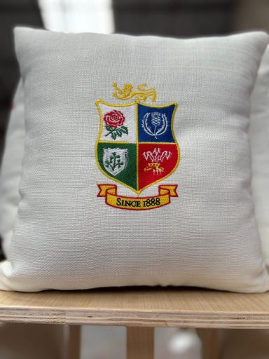 Decorative white cushion featuring a colourful shield emblem with various symbols and a ribbon.