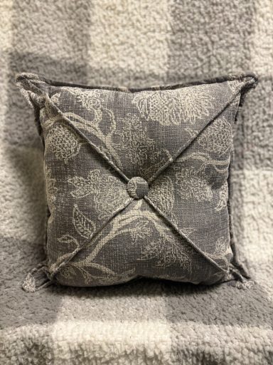 Square decorative cushion with a floral pattern and button detail, placed on a textured surface.