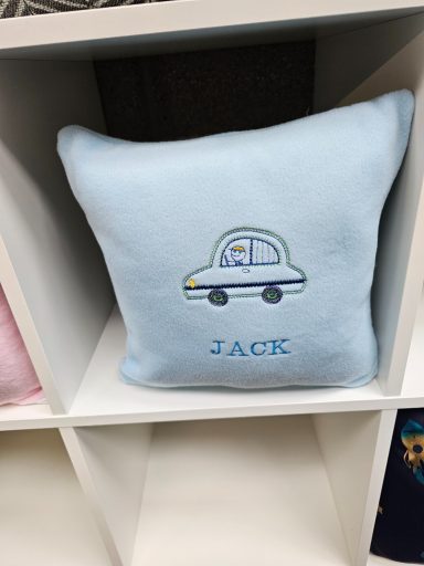 A blue cushion featuring a cartoon car and the name "JACK" embroidered. any name available 