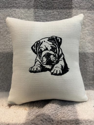 White cushion featuring a black line drawing of a crawling bulldog puppy.