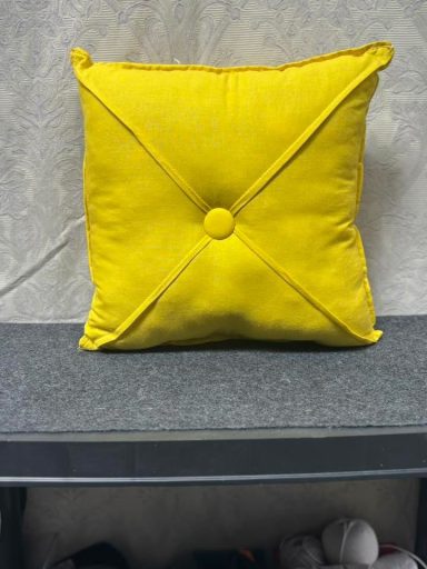 Bright yellow square pillow with a button and decorative stitching.