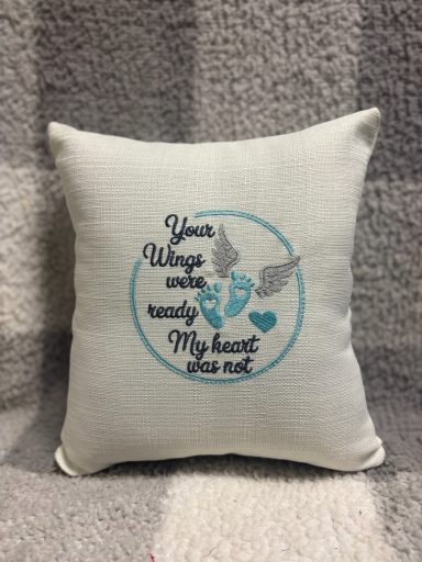 Decorative cushion with text "Your wings were ready, my heart was not" and heart graphics.