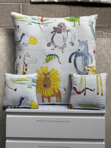 Three decorative cushions featuring playful animal illustrations on a light background.