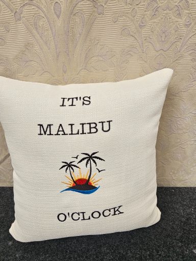 Cream cushion with the text "IT'S MALIBU O'CLOCK" and a palm tree graphic.