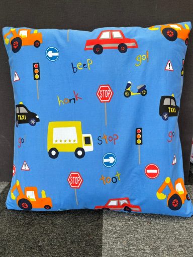 Blue cushion covered in colourful traffic-themed designs withvehicles and road signs.
