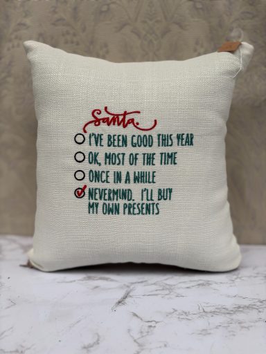 A decorative cushion with holiday-themed text about being good this year and asking for presents.