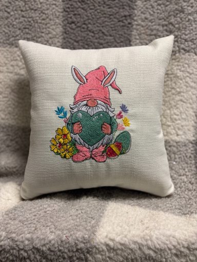 A decorative cushion featuring a rabbit with an Easter egg and flowers.