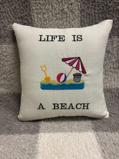 A decorative cushion with the text "Life is a Beach" and beach-themed illustrations.