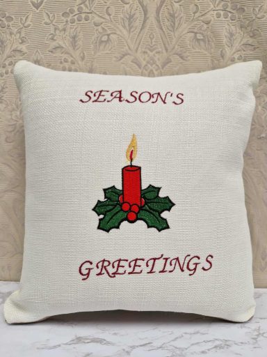 Pillow with "Season's Greetings" and a candle design surrounded by holly leaves.