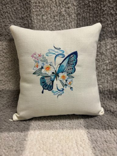 Blue butterfly and flowers embroidered on a decorative cushion.