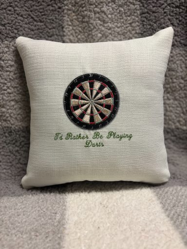 Cream cushion with a dartboard design and the text "To Make The Playing Better" underneath.